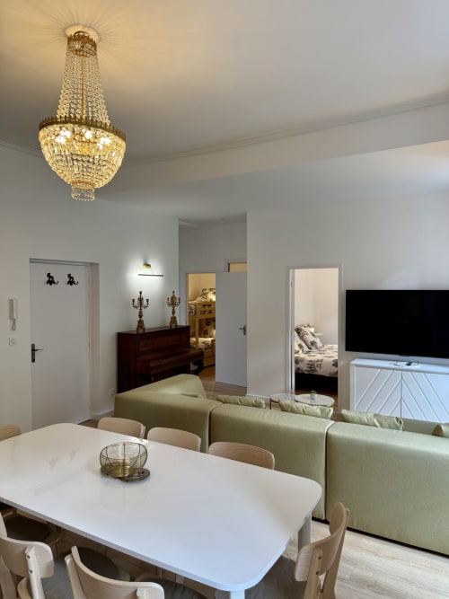 Modern apartment living room with crystal chandelier, white dining table, sage sofa, and mountain view bedroom access at Les
