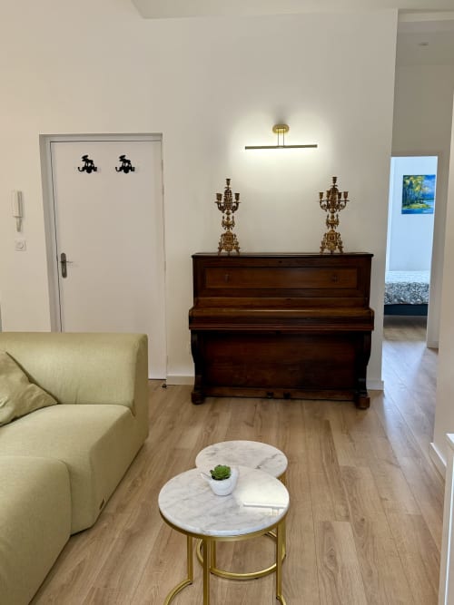 Modern living room with yellow sofa, marble table, dark wood piano, and brass candelabras in Les meublés d'Étigny apartment,