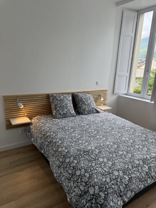 Modern bedroom with wooden slatted headboard, patterned bedding, and mountain views in Bagnères-de-Luchon apartment