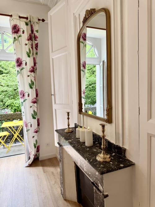 Elegant hallway at Les meublés d'Étigny with black marble console, ornate gold mirror, floral curtains, and mountain views