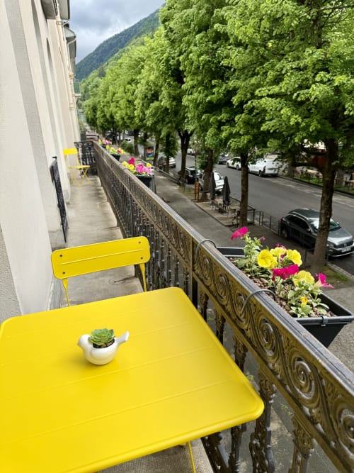 Bright yellow balcony furniture with potted flowers overlooking Bagnères-de-Luchon street and mountains