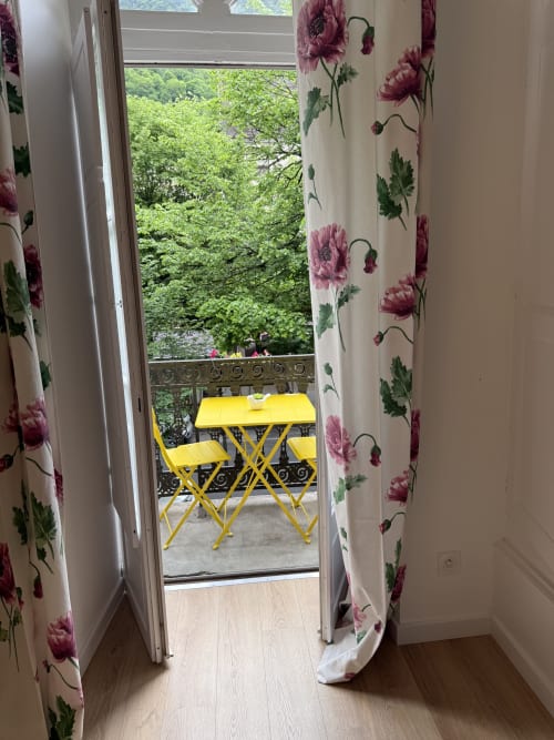 Open balcony door at Les meublés d'Étigny showing yellow outdoor furniture and lush mountain views in Bagnères-de-Luchon