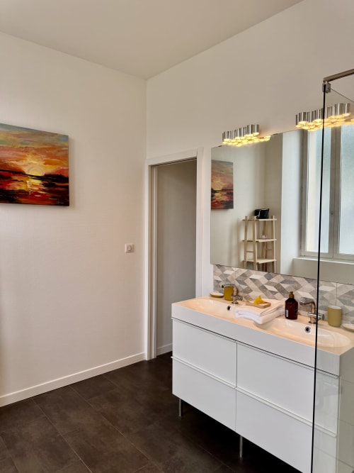 Modern bathroom with white vanity, large mirror, and heated lighting at Les meublés d'Étigny apartment in Bagnères-de-Luchon