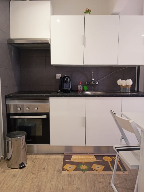 Cozinha moderna com armários brancos, bancada preta, eletrodomésticos em aço inoxidável, pia e piso de madeira em Sweet Home