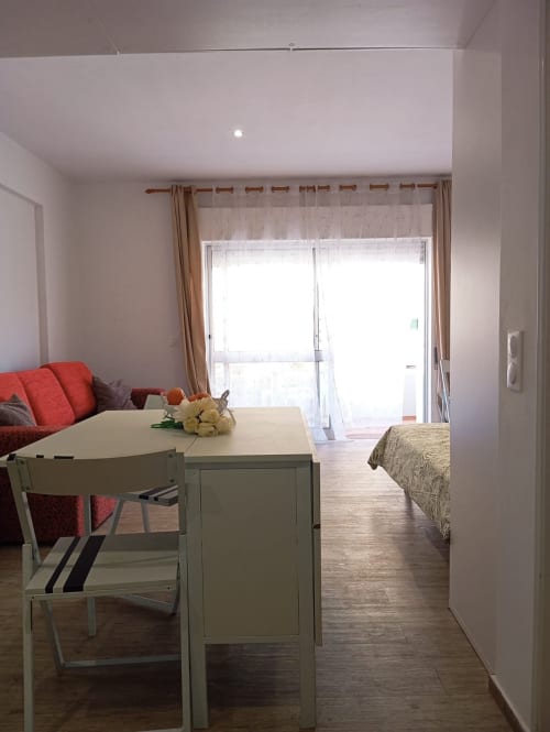Moderna sala de estar de apartamento com mesa de jantar, sofá vermelho e portas de vidro que abrem para varanda em Portimão