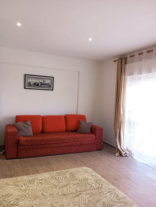 Sala de estar luminosa com sofá vermelho, piso em madeira e acesso à varanda no apartamento Sweet Home, Portimão