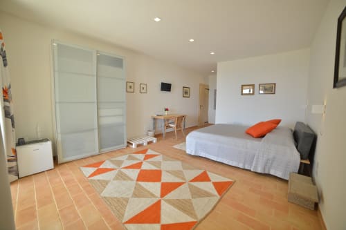 Luminosa camera doppia superior dell'hotel Proprietà Clara ad Assisi con letto, scrivania, tappeto geometrico arancione e porta scorrevole moderna