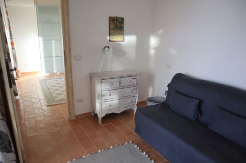 Camera luminosa della Proprietà Clara ad Assisi con divano blu navy, cassettone bianco, pavimenti in cotto e luce naturale