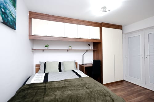 Modern bedroom in Salford apartment with wooden bed frame, white pillows, striped bedding, built-in storage, and desk area