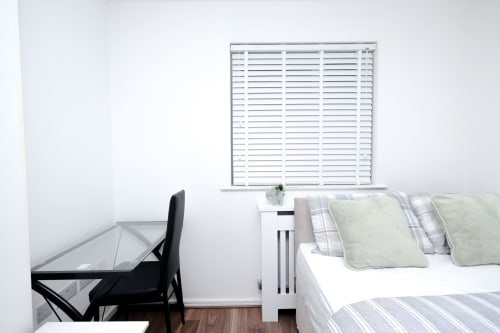 Modern bedroom with desk, black chair, white shutters, and bed with patterned pillows in Salford apartment