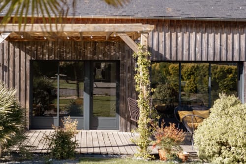 Terrasse en bois contemporaine au Manoir de la Nogrie avec transats, lierre grimpant et architecture moderne à Val d'Izé.