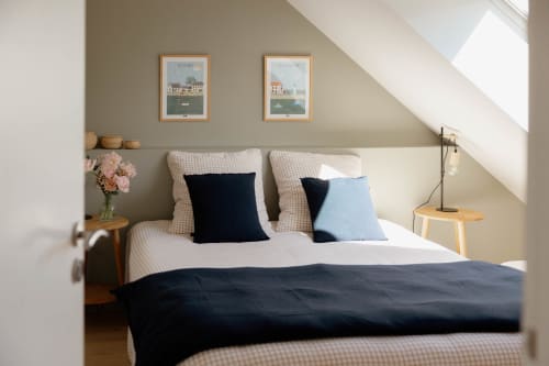 Chambre mansardée lumineuse au Manoir de la Nogrie avec gravures marines, accents bleu marine et lumière naturelle par fenêtre de toit.