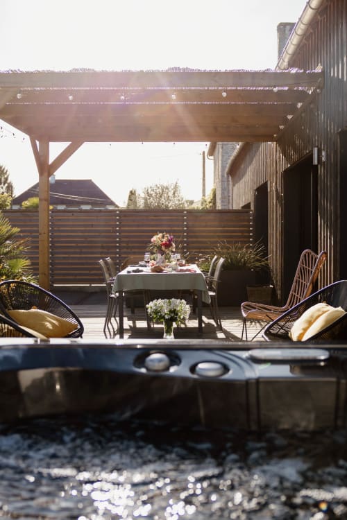 Élégante terrasse extérieure au Manoir de la Nogrie avec table à manger, chaises en rotin, pergola et foyer