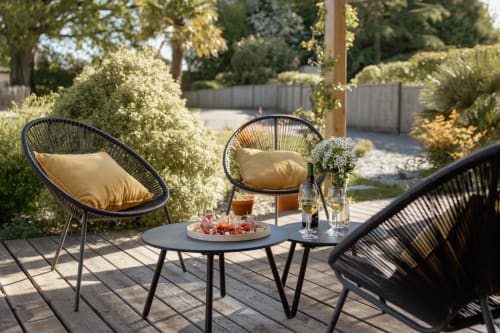 Élégante terrasse extérieure du Manoir de la Nogrie avec fauteuils tressés rembourrés, amuse-bouches et vue sur le jardin.