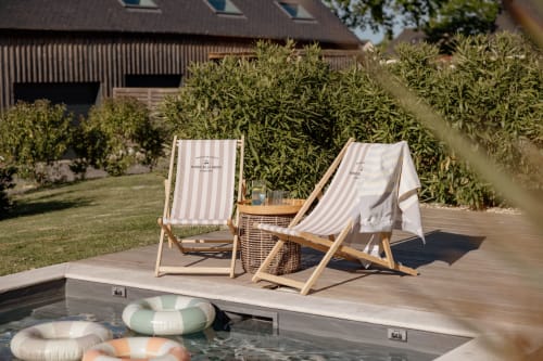 Deux chaises longues rayées au bord de la piscine du Manoir de la Nogrie en Val d'Izé, avec haies et grange en arrière-plan