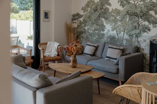 Salon moderne du Manoir de la Nogrie avec canapés gris, table basse en bois et fresque murale nature à Val d'Izé