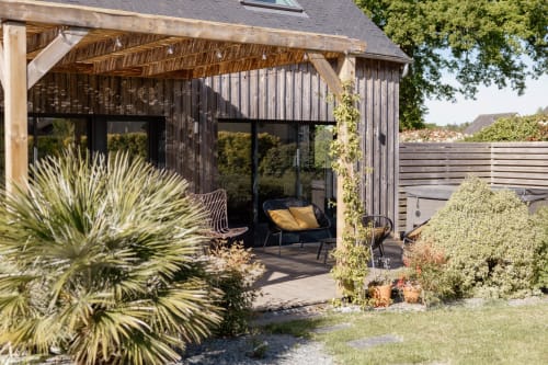 Modern pergola-covered terrace at La Grange cottage with lounge seating, garden views, and ivy-draped wooden structure in Val