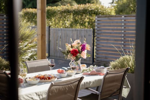 Sunny garden dining setup at Manoir de la Nogrie cottage with floral centerpiece, wine glasses, and outdoor furniture on