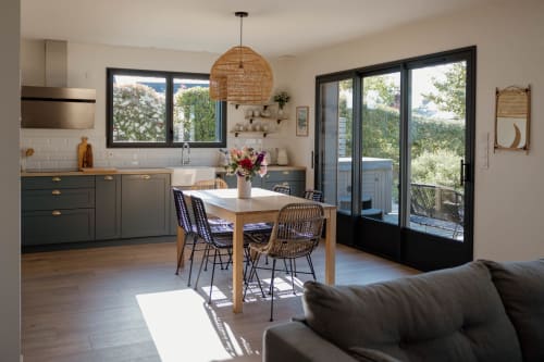 Modern open-plan kitchen and dining area in La Grange cottage with garden views, featuring dark cabinetry, wooden table, and