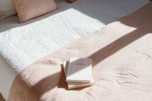 Stacked books on pink bedding in La Grange cottage at Manoir de la Nogrie with white pillows and garden views