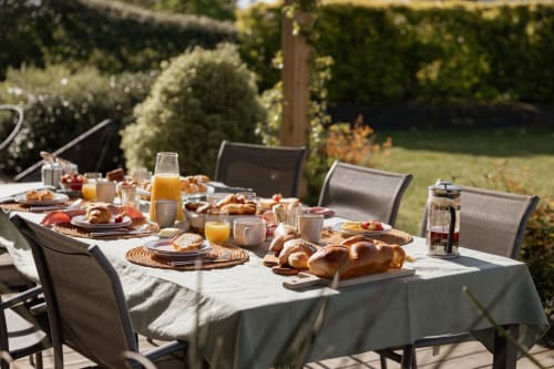 Outdoor breakfast setup at Manoir de la Nogrie cottage with pastries, juice, and garden views