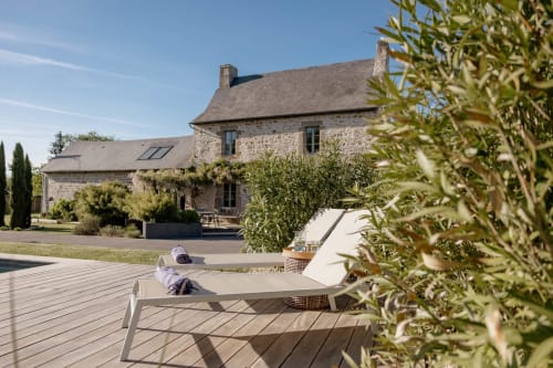 Stone cottage with deck seating, olive plants, and countryside views at Manoir de la Nogrie, Val d'Izé