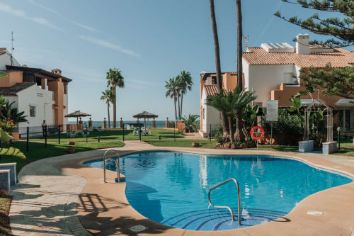 Curved swimming pool with sea views at BH Marbella resort in Spain, featuring Mediterranean-style buildings and palm trees