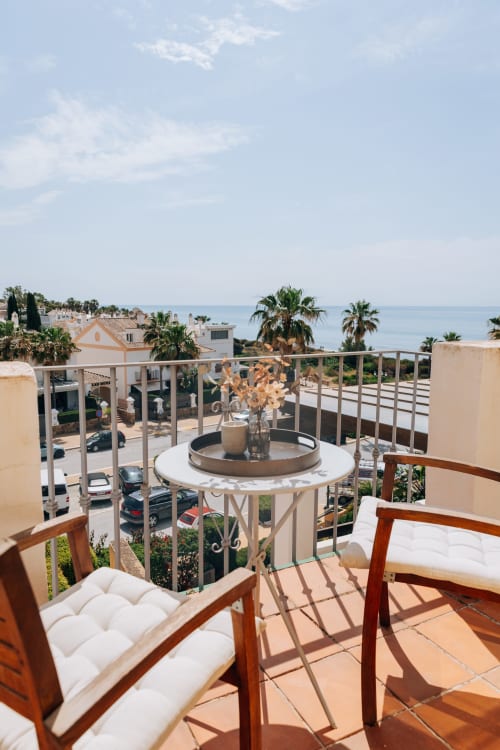 Terrace at Stromboli triplex in Marbella with sea view, round table, wooden chairs, and Mediterranean coastline beyond.