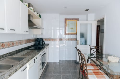 Modern kitchen in Stromboli triplex apartment at BH Marbella with white cabinets, granite counters, and dining area
