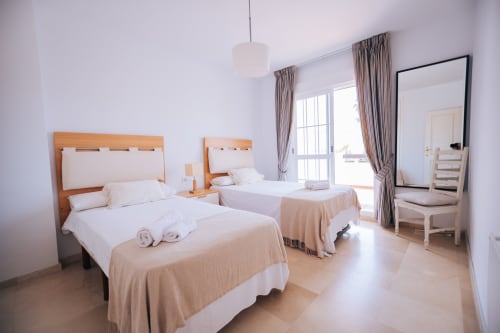 Bright bedroom with two beds, wooden headboards, white linens, sea-view balcony, and modern amenities at BH Marbella hotel in
