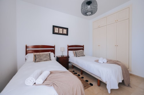 Twin bedroom in Stromboli triplex apartment at BH Marbella with wooden beds, white linens, and cream wardrobe storage.