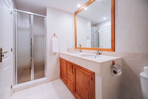 Modern bathroom with wooden vanity, dual sinks, large mirror, and glass shower enclosure at BH Marbella apartment in Marbella