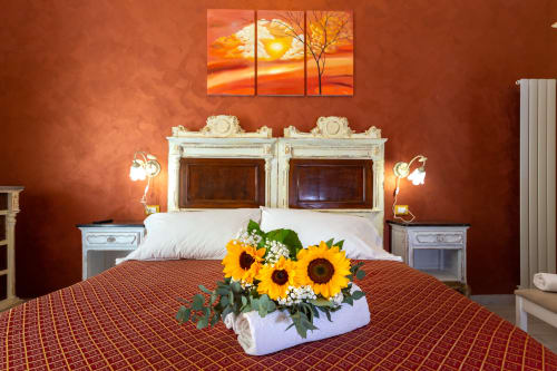Camera Lina presso Casa Scola Loano con pareti in terracotta, testata ornamentale, composizione di girasoli e quadri con tramonto caldo