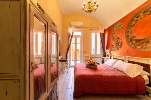 Camera Pippo della Casa Scola Loano B&B con letto coperto di rosso, pareti gialle, opere d'arte arancioni e design moderno