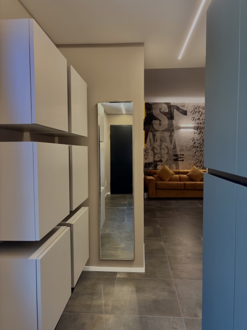 Corridoio moderno della Suite Sibilla a Manu Maison, Parma, con armadiature bianche minimaliste, specchio, pavimenti scuri e zona living