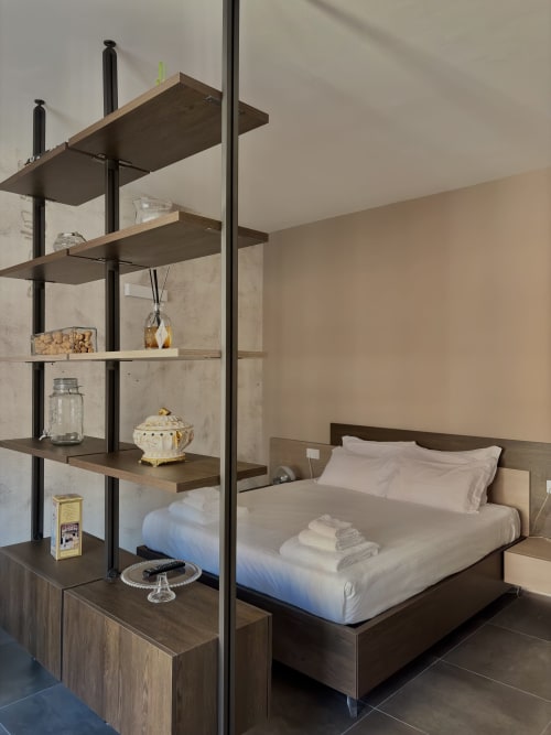 Camera della Suite Sibilla a Parma con scaffalature in legno, letto queen size, biancheria bianca e mobili moderni in legno scuro
