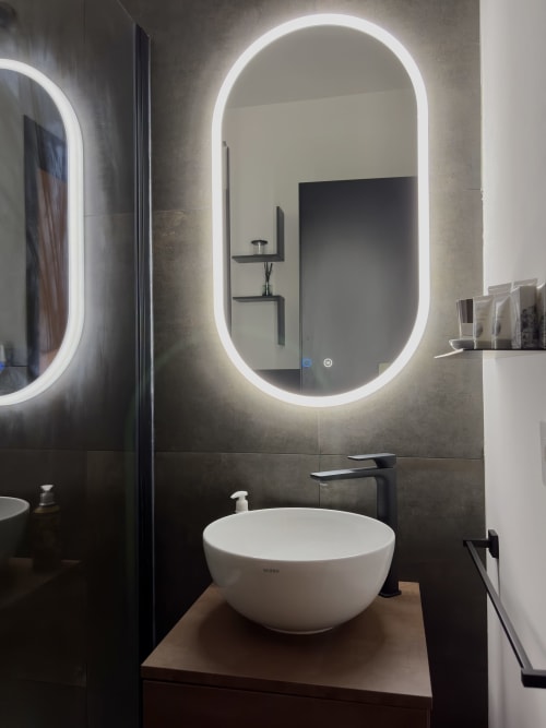 Bagno moderno nella Sibilla Suite di Manu Maison Parma, con specchio LED ovale, lavabo bianco a ciotola e pareti rivestite in piastrelle scure