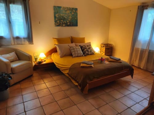 Chambre chaleureuse au Domaine Bellavigne avec murs jaunes, lits jumeaux, fauteuil, carrelage en terre cuite et éclairage ambiant