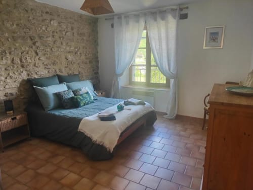 Chambre spacieuse au Domaine Bellavigne avec murs en pierre, literie bleue, grandes fenêtres, mobilier en bois et carrelage en terre cuite