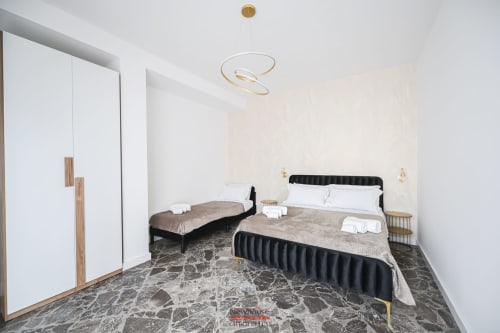 Cavour Deluxe apartment bedroom in Bari with twin beds, black headboards, modern ceiling light, wardrobe, and patterned floor
