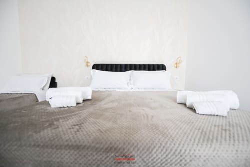 Camera da letto Cavour Deluxe a Newhouse Bari con testata nera, cuscini bianchi, biancheria grigia e applique dorate