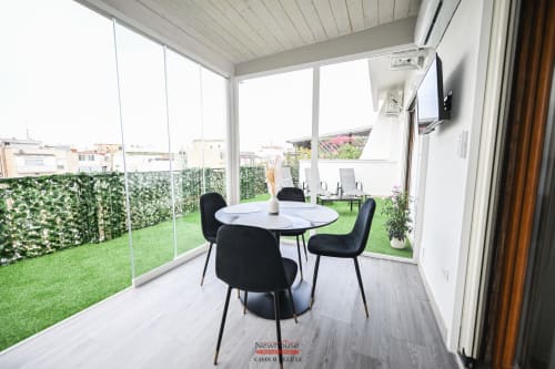Balcone dell'appartamento Cavour Deluxe a Bari con tavolo da pranzo, sedie nere, erba sintetica e vista sulla città attraverso il vetro