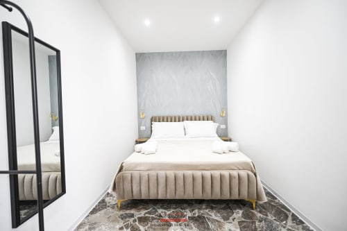 Newhouse Cavour Deluxe room in Bari featuring a contemporary beige upholstered bed with white pillows and marble flooring
