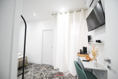 Spazioso angolo di lavoro nella moderna camera d'albergo con TV a schermo piatto, scrivania con sedia e pavimento in marmo bianco presso l'Newhouse Bari