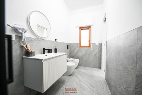 Bagno moderno nella camera Newhouse Cavour Deluxe a Bari. Piastrelle in marmo grigio, lavabo bianco, specchio rotondo, water