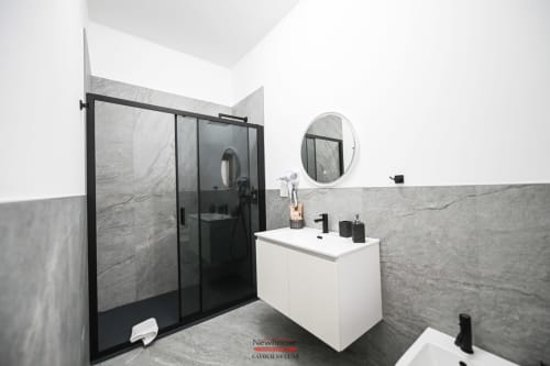Bagno moderno nella suite Newhouse Cavour Deluxe di Bari - pareti in marmo, doccia con telaio nero, vanity bianca, specchio rotondo