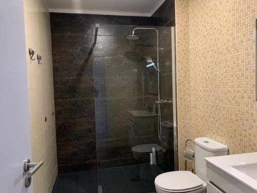 Banheiro moderno na Estação Boutique Campanhã no Porto com box de vidro, azulejos escuros nas paredes, pia branca e