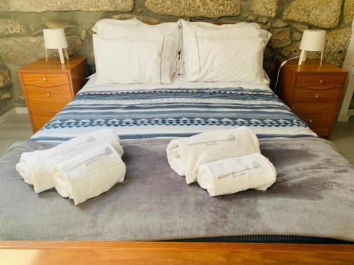 Bedroom at Campanhã Boutique in Porto with bed, white pillows, blue striped blanket, rolled towels, and wooden nightstands