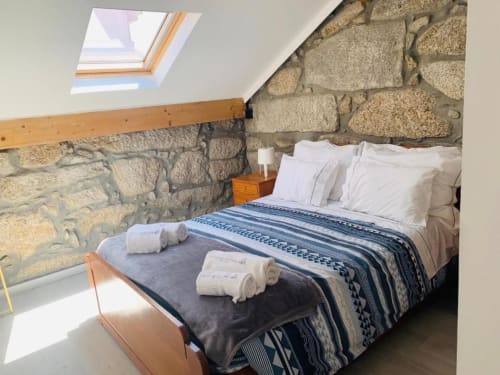 Cozy attic bedroom at Campanhã Boutique Station Porto with exposed stone walls, skylight, and neatly arranged bed with white