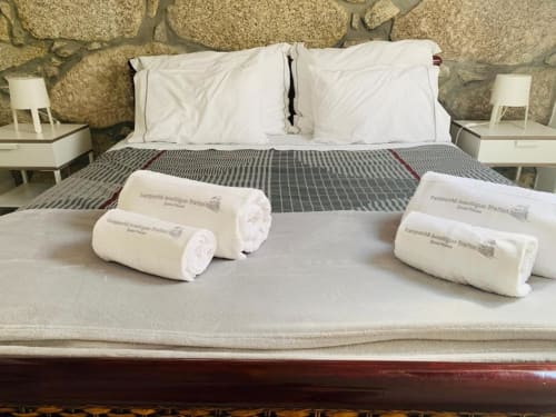 White rolled towels on bed at Campanhã Boutique Station hotel in Porto, with white pillows and gray bedding against stone